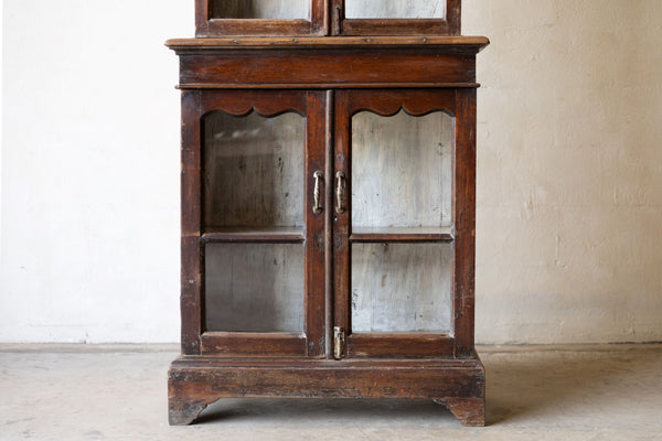 Bottom of vintage wooden cabinet with glass doors against a plain wall.