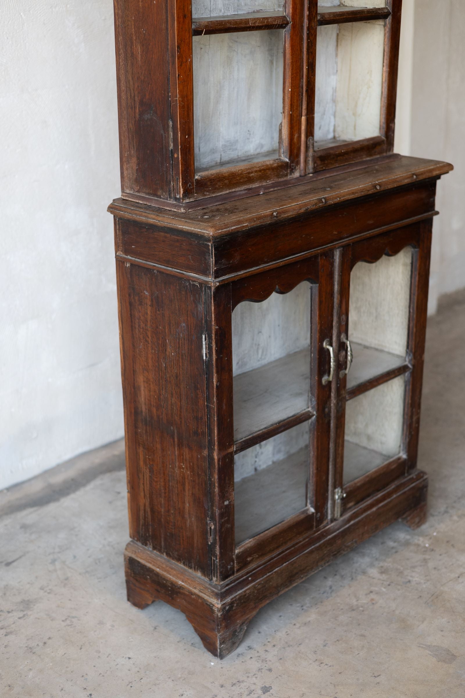Wooden cabinet with glass doors in a room with white walls and a concrete floor.