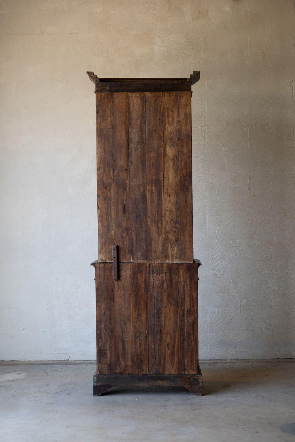 Back of vintage wooden bookcase against a plain wall.