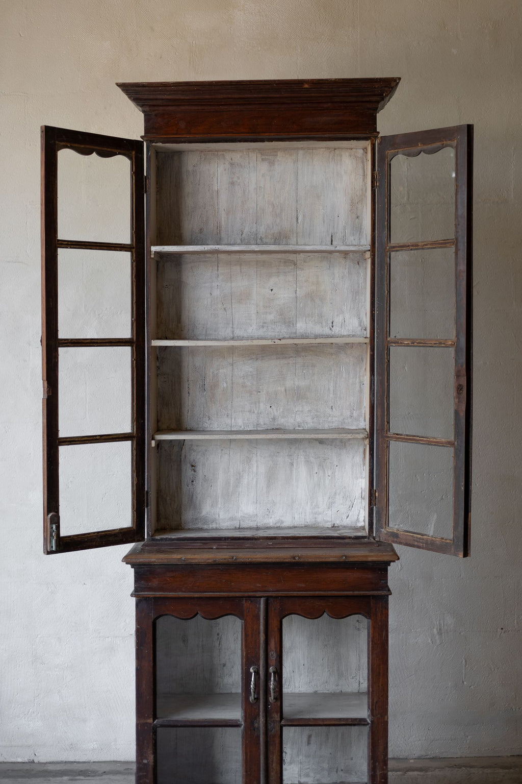 Wooden cabinet with open glass doors against a plain wall