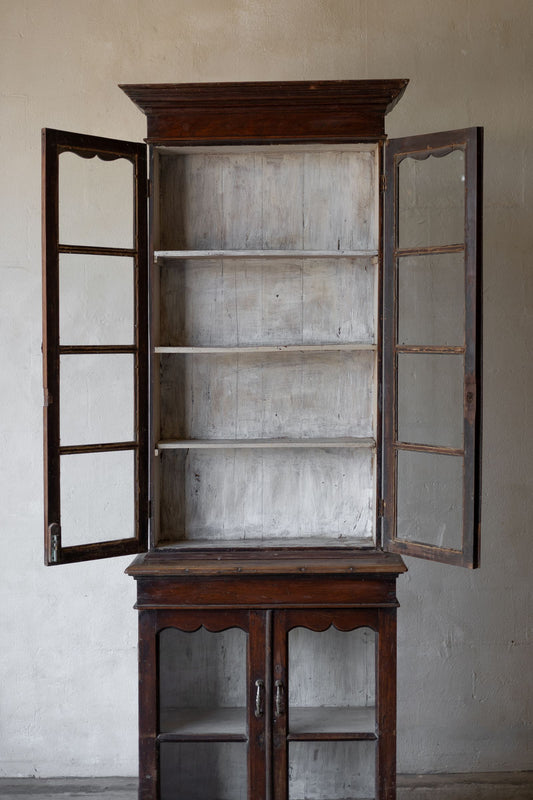Wooden cabinet with open glass doors against a plain wall