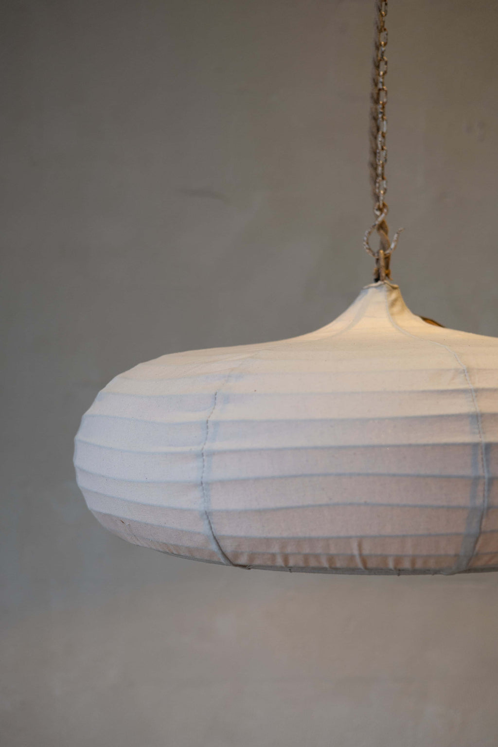 Partial image of a teardrop pendant light with off-white woven canvas and rope and chain cord.