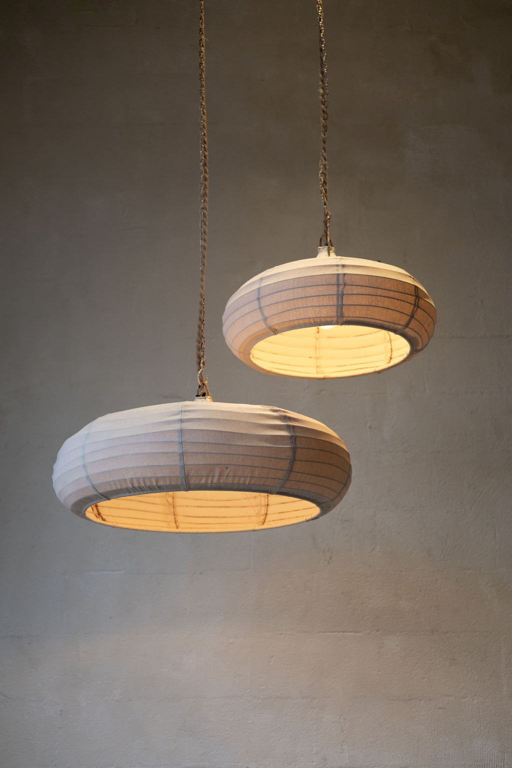 Low angle of two teardrop pendant lights with off-white woven canvas and rope and chain cords.