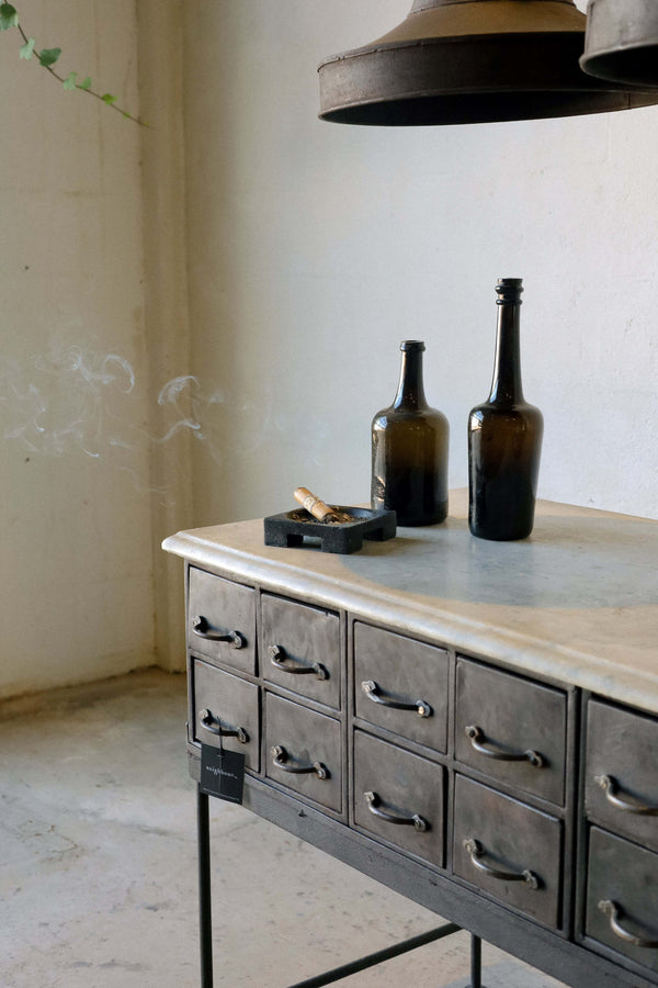 A square cast iron cigar tray on a marble-top console.