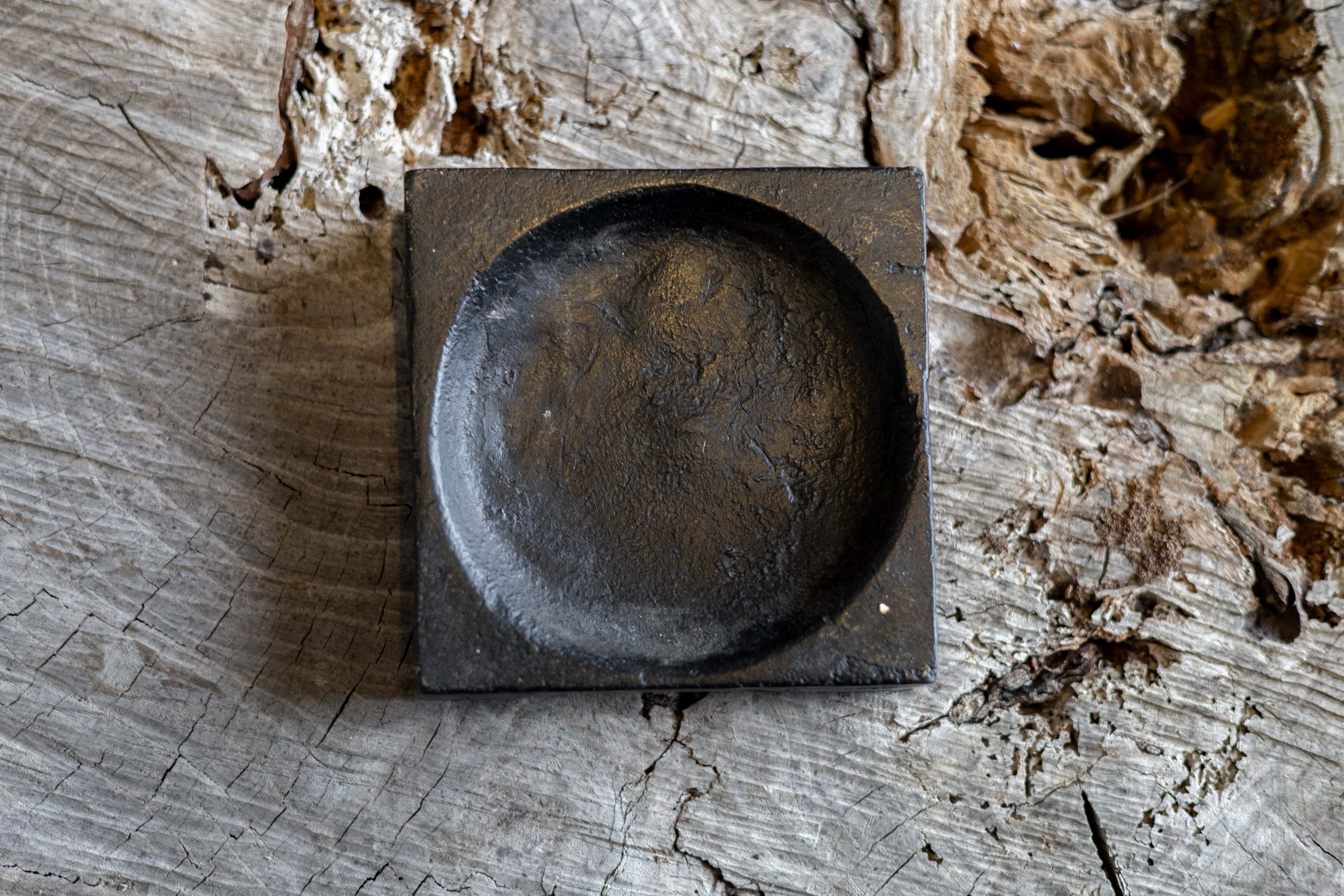 A black, square cast iron cigar tray with a circular indentation. 
