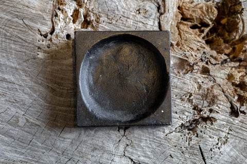 A black, square cast iron cigar tray with a circular indentation. 