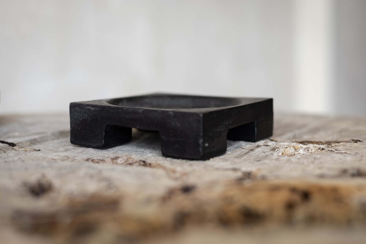 Side view of a black cast iron cigar tray with block leg design.