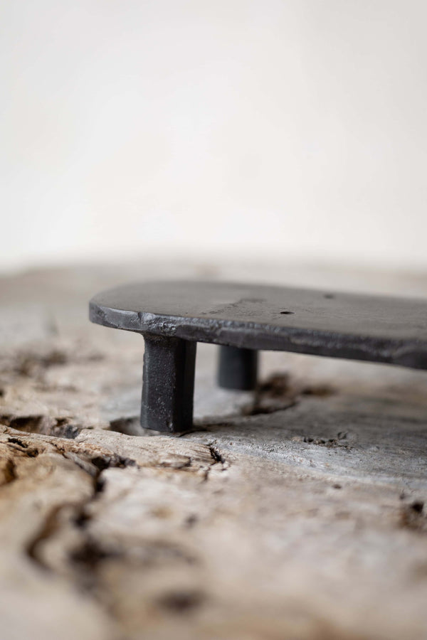 A black, oval cast iron soap stand on a worn wooden surface.