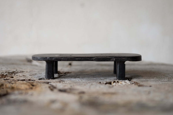 A black, oval cast iron soap stand on a worn wooden surface