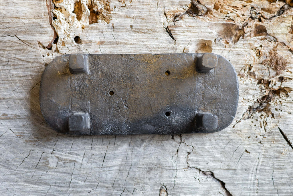 Upside down black, oval cast iron soap stand on a worn wooden surface. The soap stand has three small holes for drainage.