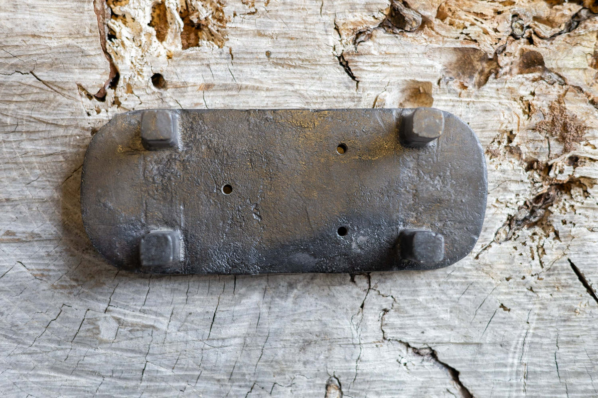 Upside down black, oval cast iron soap stand on a worn wooden surface. The soap stand has three small holes for drainage.