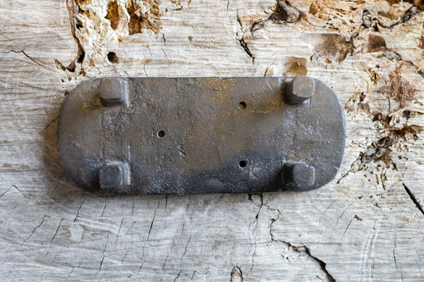 Upside down black, oval cast iron soap stand on a worn wooden surface. The soap stand has three small holes for drainage.