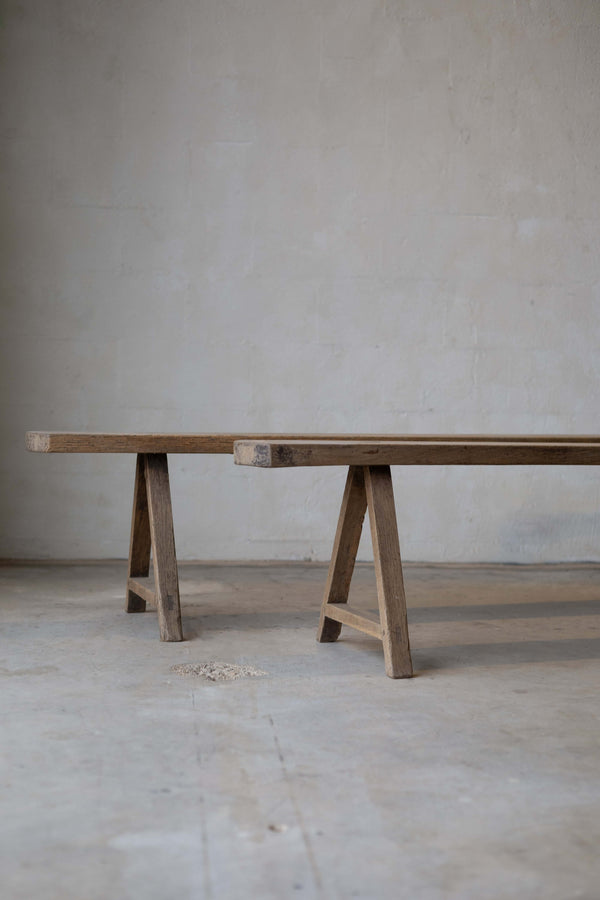 Partial view of two long, thin, wooden dining benches, with simple A-frame.