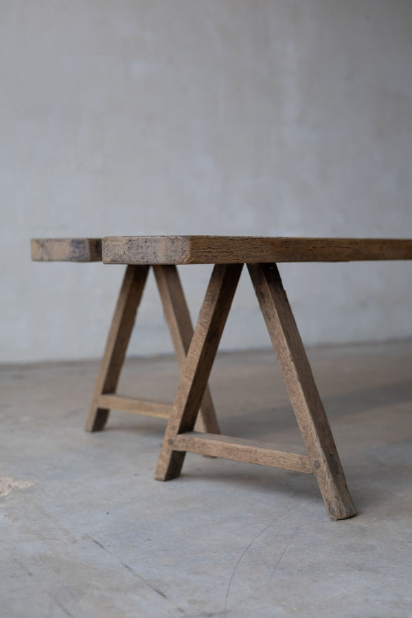Partial staggered view of two long, thin, wooden dining benches, with simple A-frame.