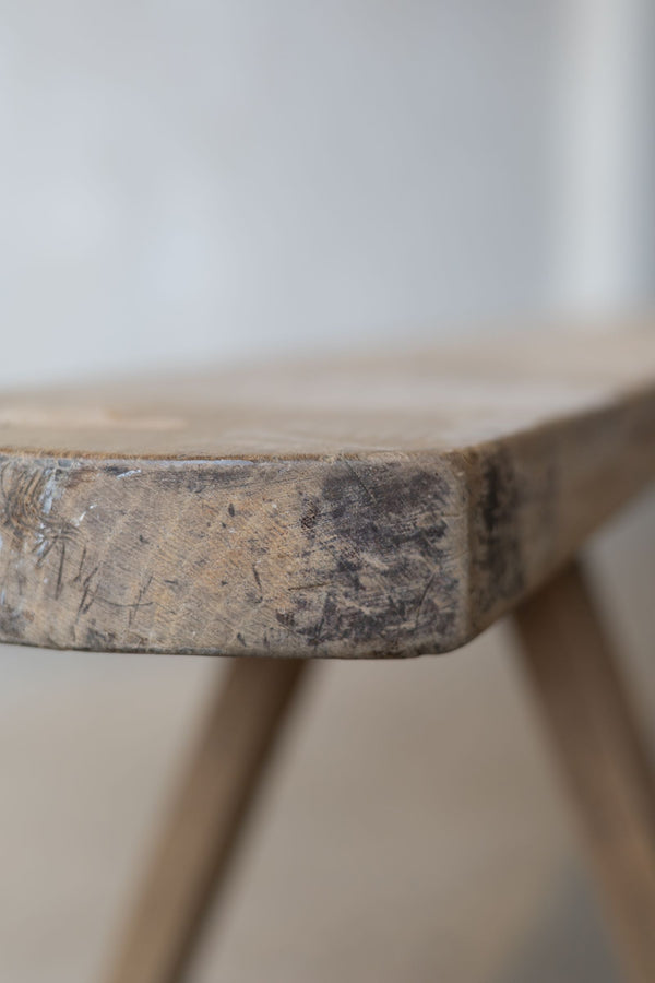 Close-up view of the side of a thin, wooden dining bench, featuring natural, rustic wood finish.
