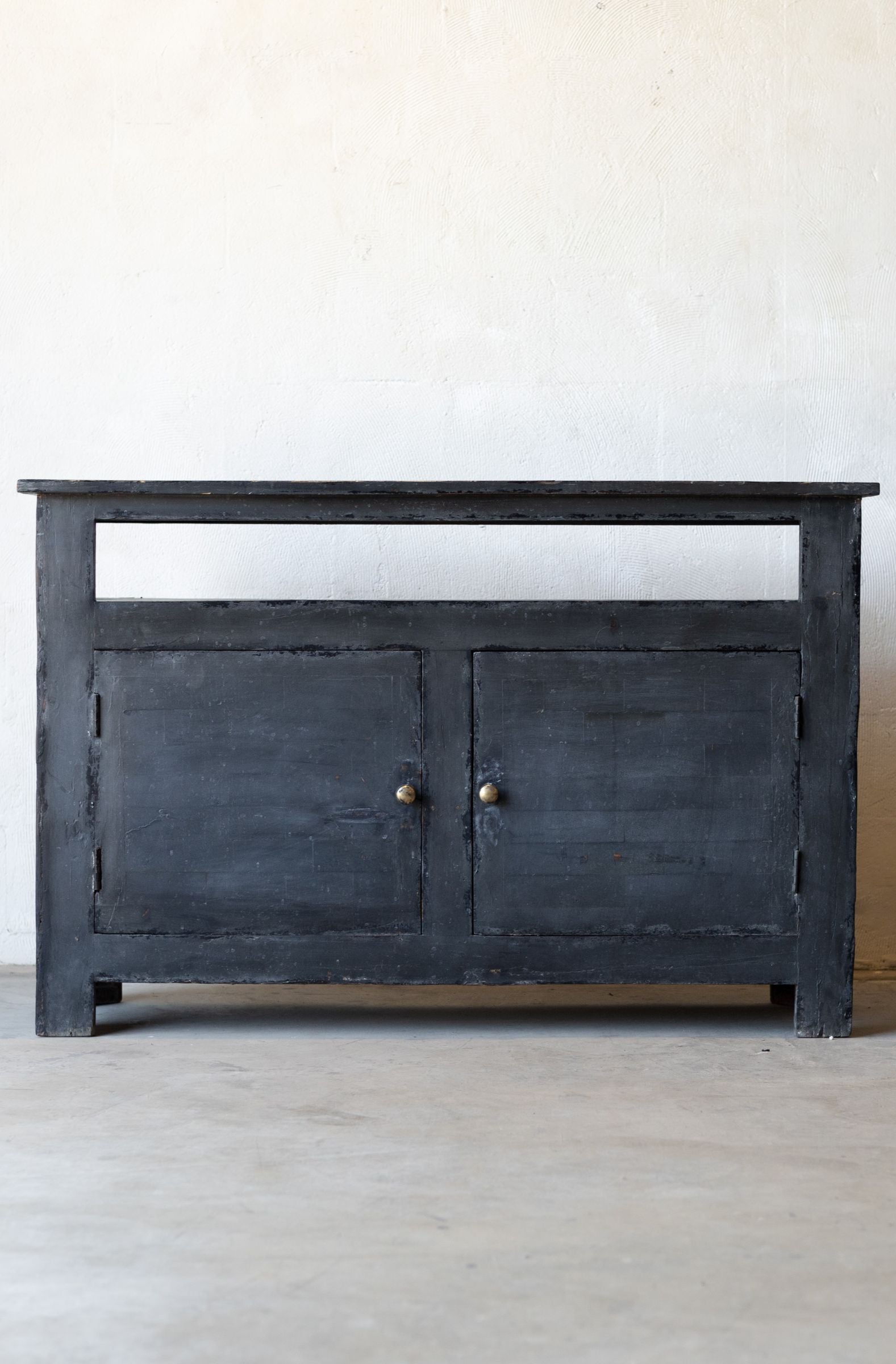 Dark wooden console table with two doors on a light gray floor and white wall background.