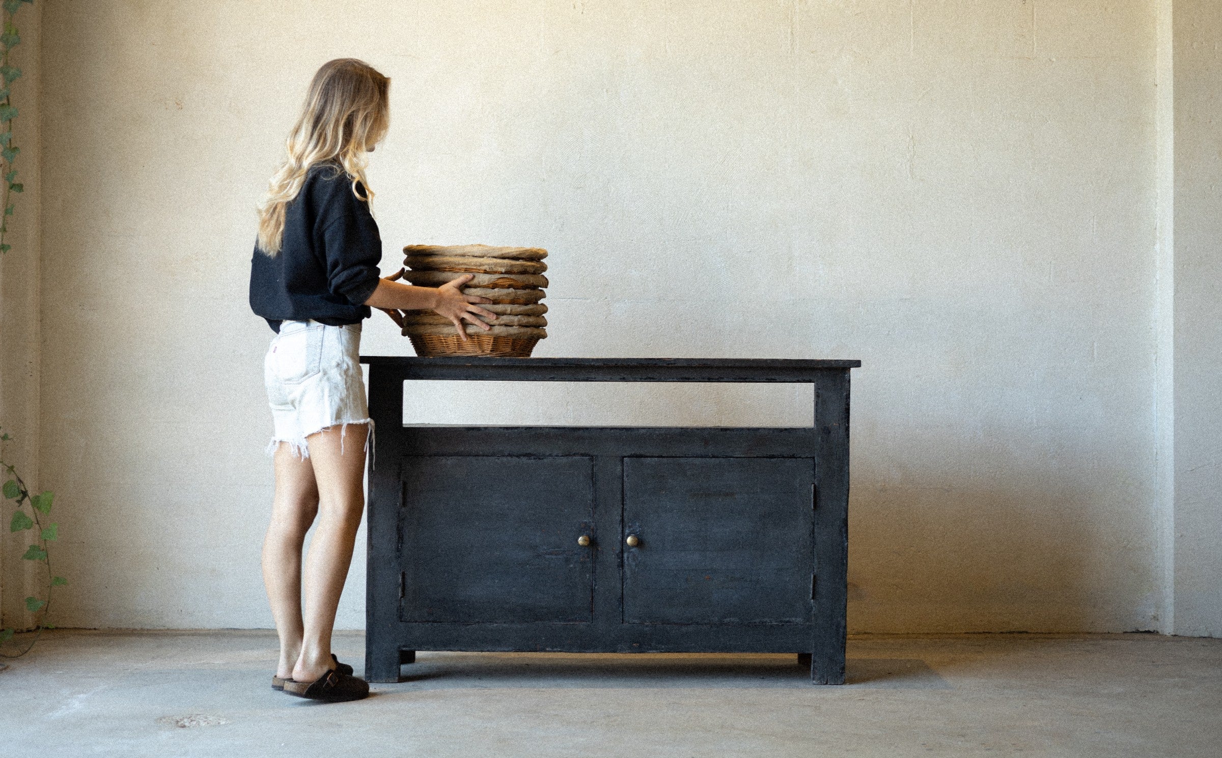 Woman arranging baskets on a black wooden console cabinet in a minimalistic room.