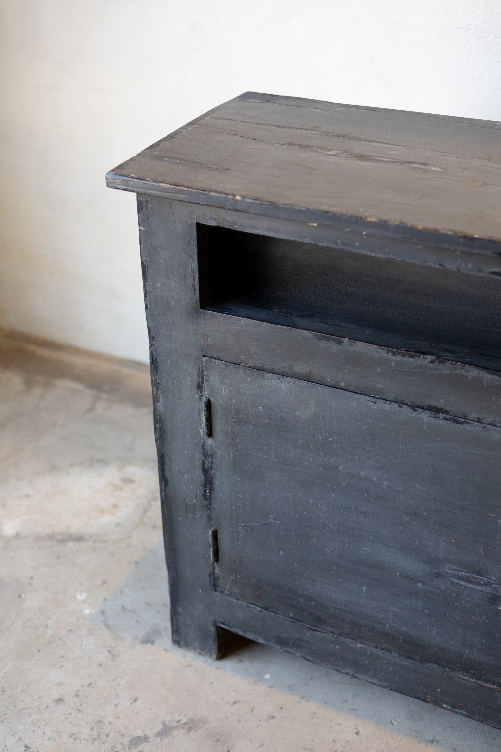 Left side of dark wooden sideboard on a light gray floor against a white wall.