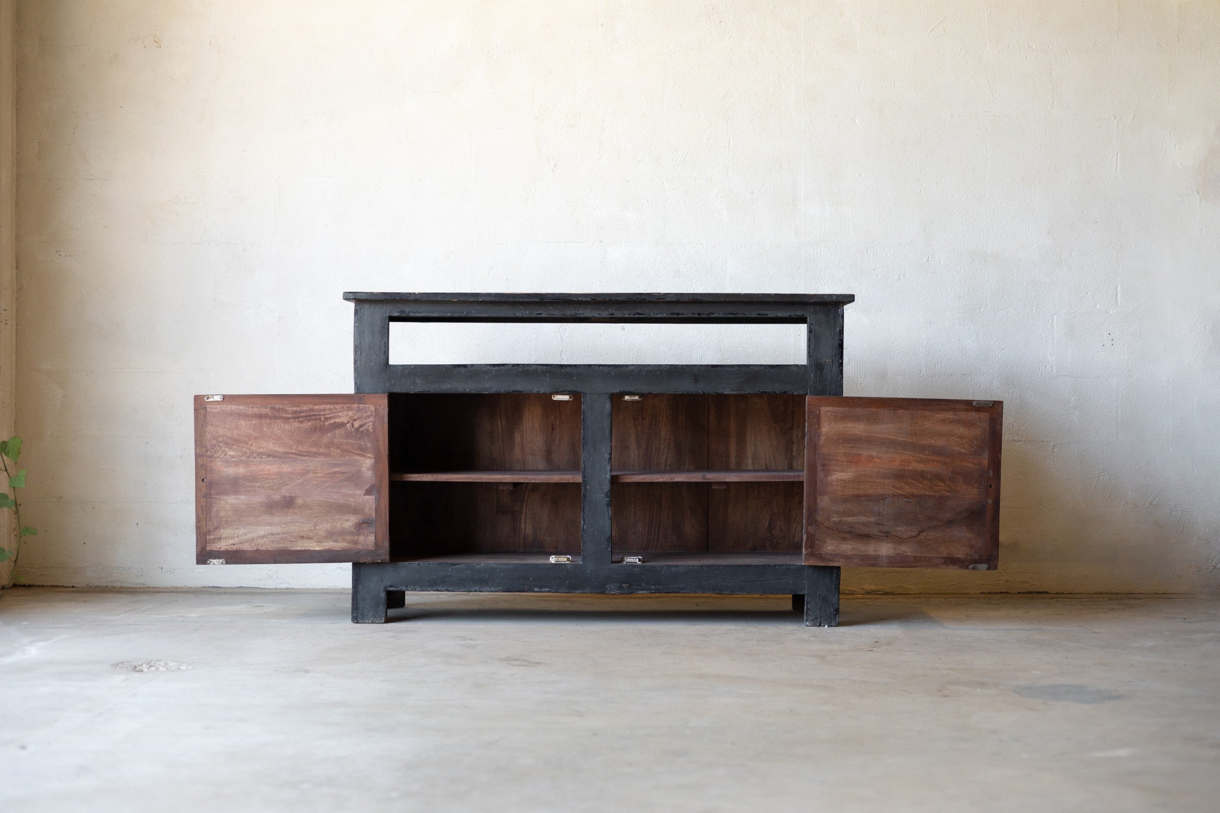 Dark wooden console with cabinet two doors open revealing two shelves for storage on each side against a plain wall.