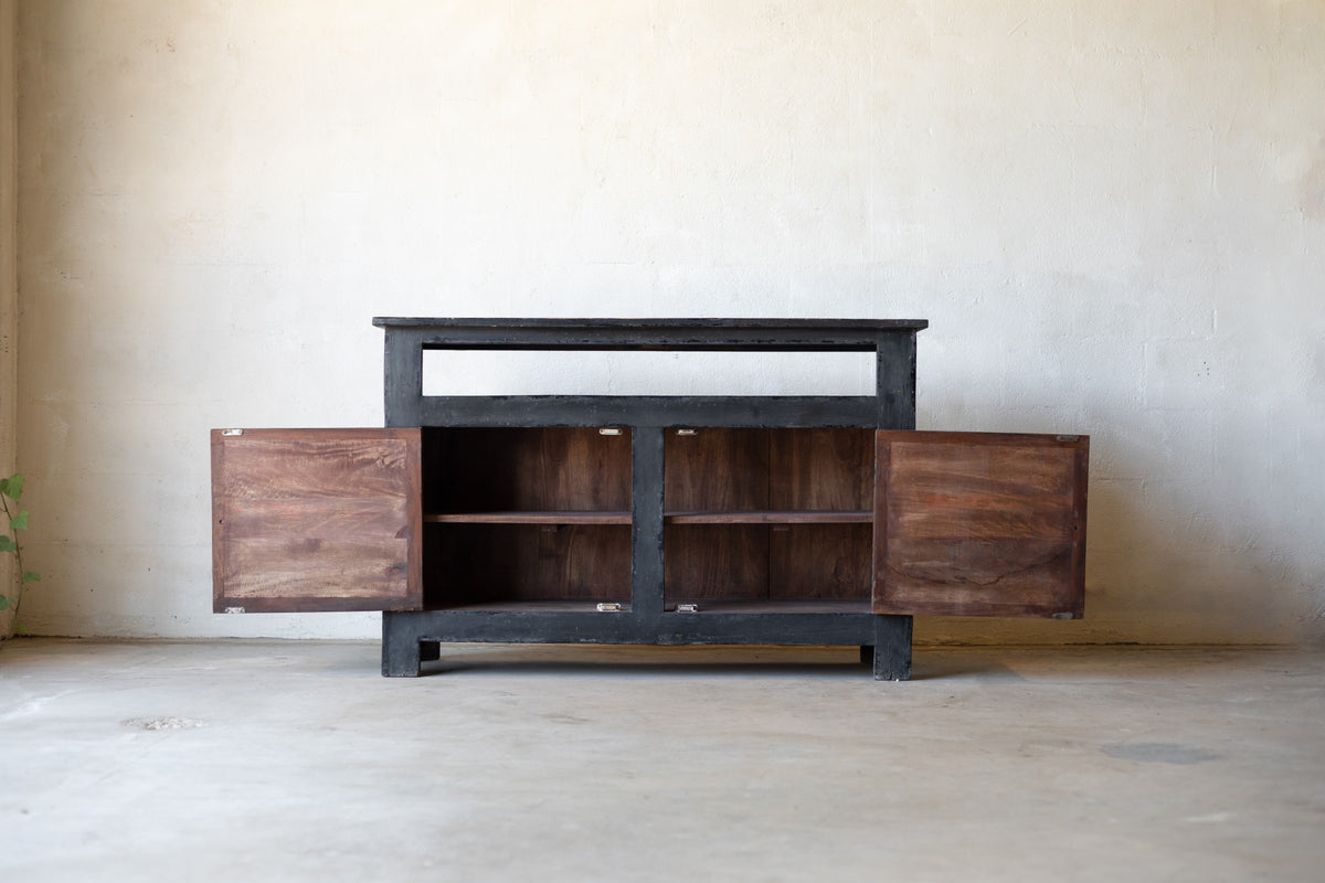 Dark wooden console with cabinet two doors open revealing two shelves for storage on each side against a plain wall.