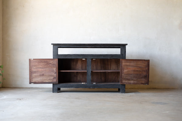 Dark wooden console with cabinet two doors open revealing two shelves for storage on each side against a plain wall.