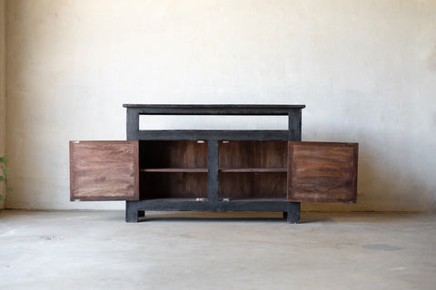 Dark wooden console with cabinet two doors open revealing two shelves for storage on each side against a plain wall.