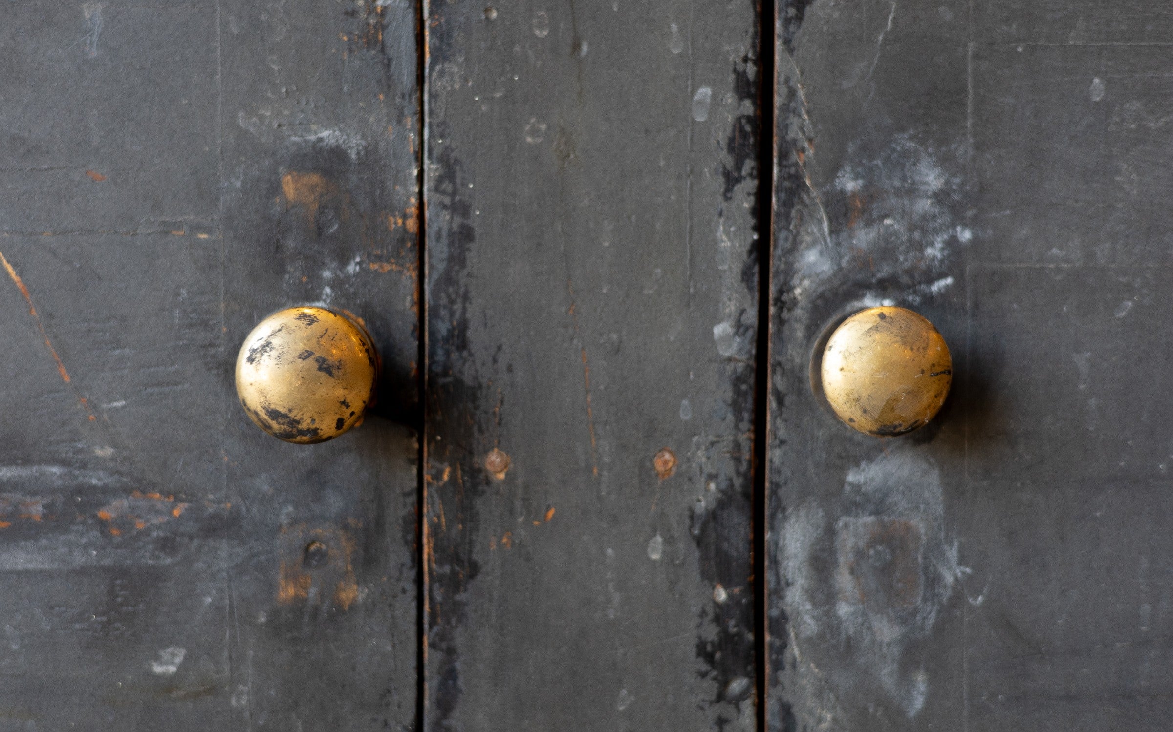 Close-up of a dark wooden console cabinet door with two golden doorknobs.