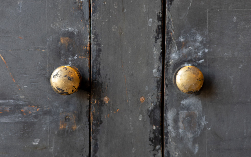 Close-up of a dark wooden console cabinet door with two golden doorknobs.
