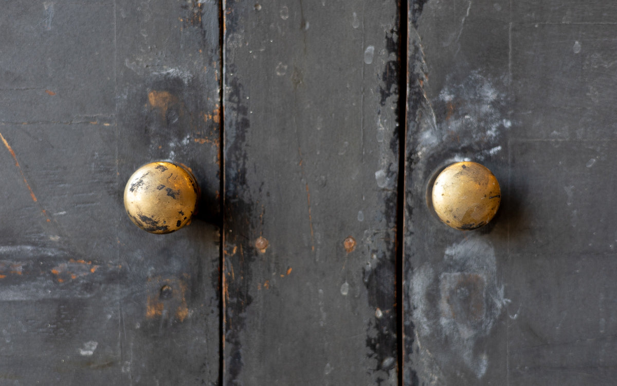 Close-up of a dark wooden console cabinet door with two golden doorknobs.