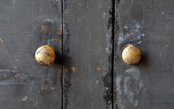 Close-up of a dark wooden console cabinet door with two golden doorknobs.