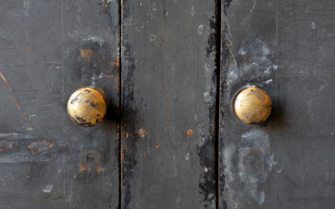 Close-up of a dark wooden console cabinet door with two golden doorknobs.
