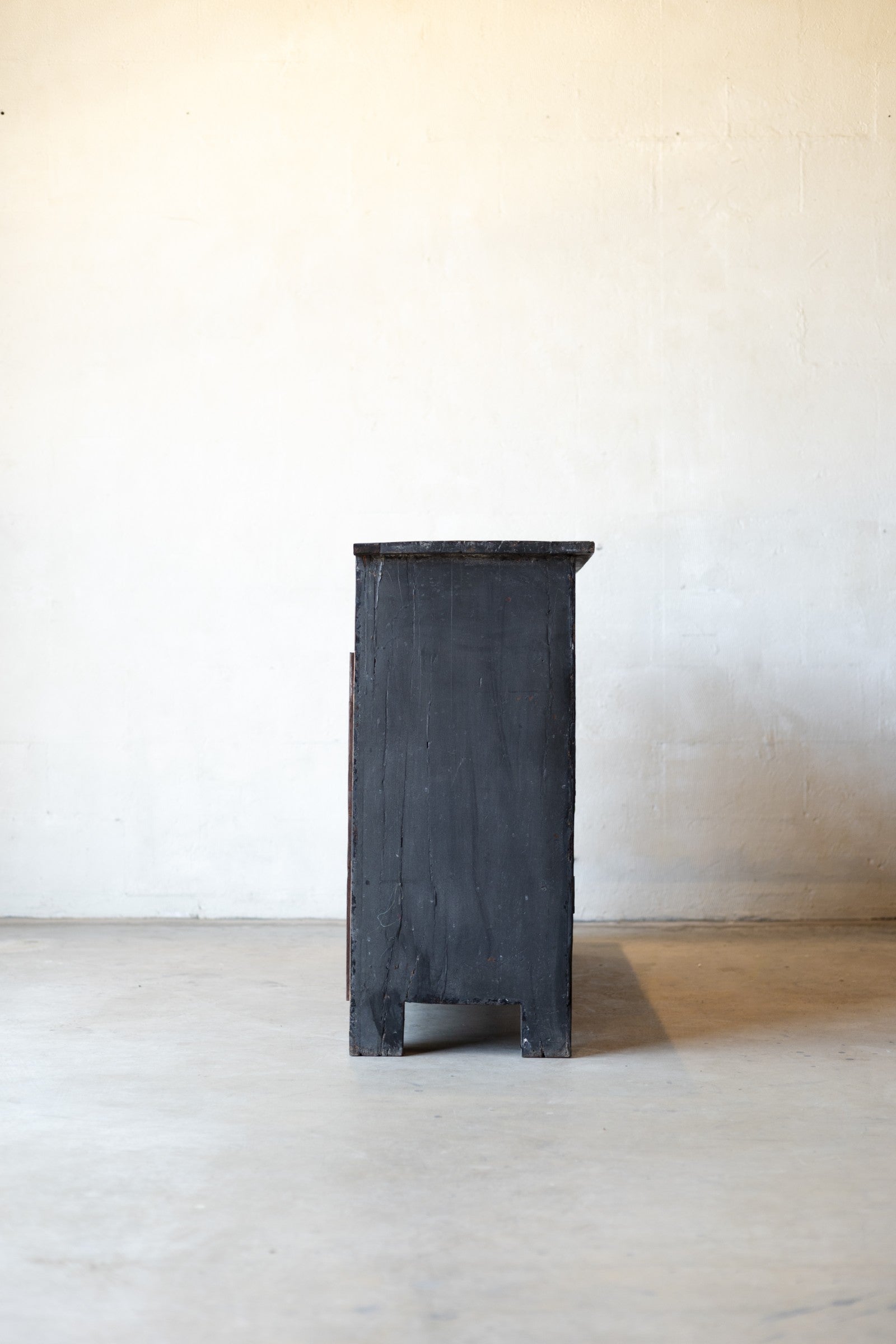 Side angle of back wooden console table on a light wooden floor with a white wall background.