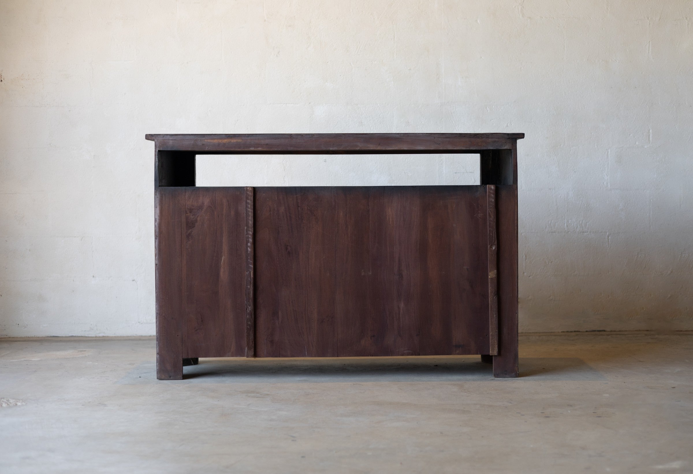 Back of wooden sideboard cabinet against a plain wall.