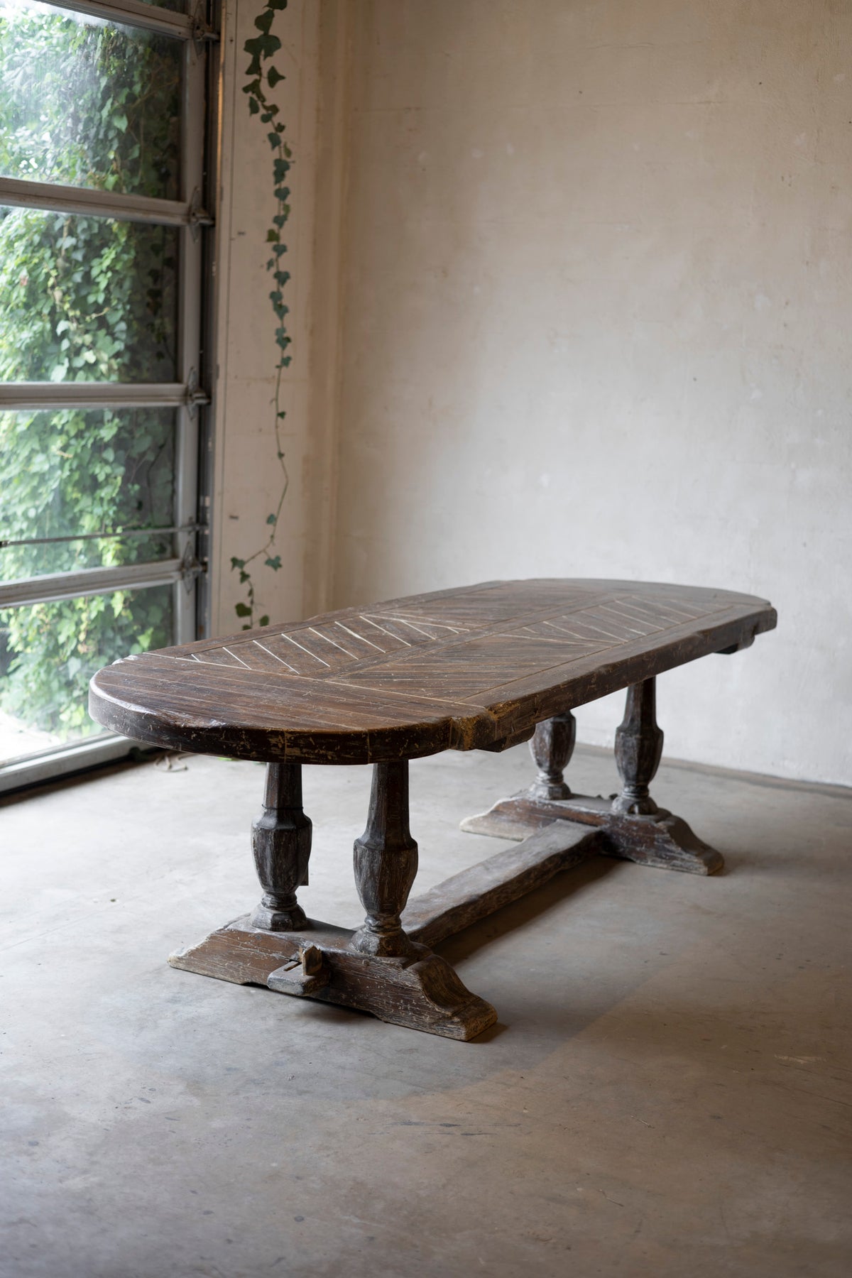 Vintage wooden table in a room with large windows and a white wall.