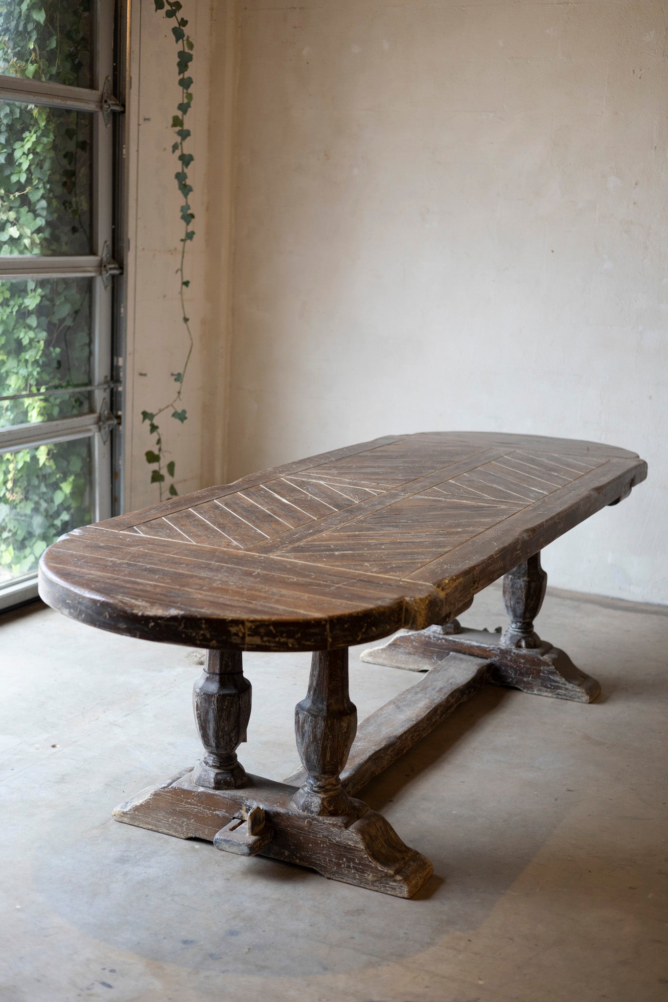 Wooden table with a chevron pattern in a room with a window and ivy.