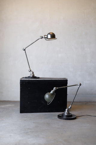 Two vintage Jielde desk lamps on a black rectangular block against a plain wall.