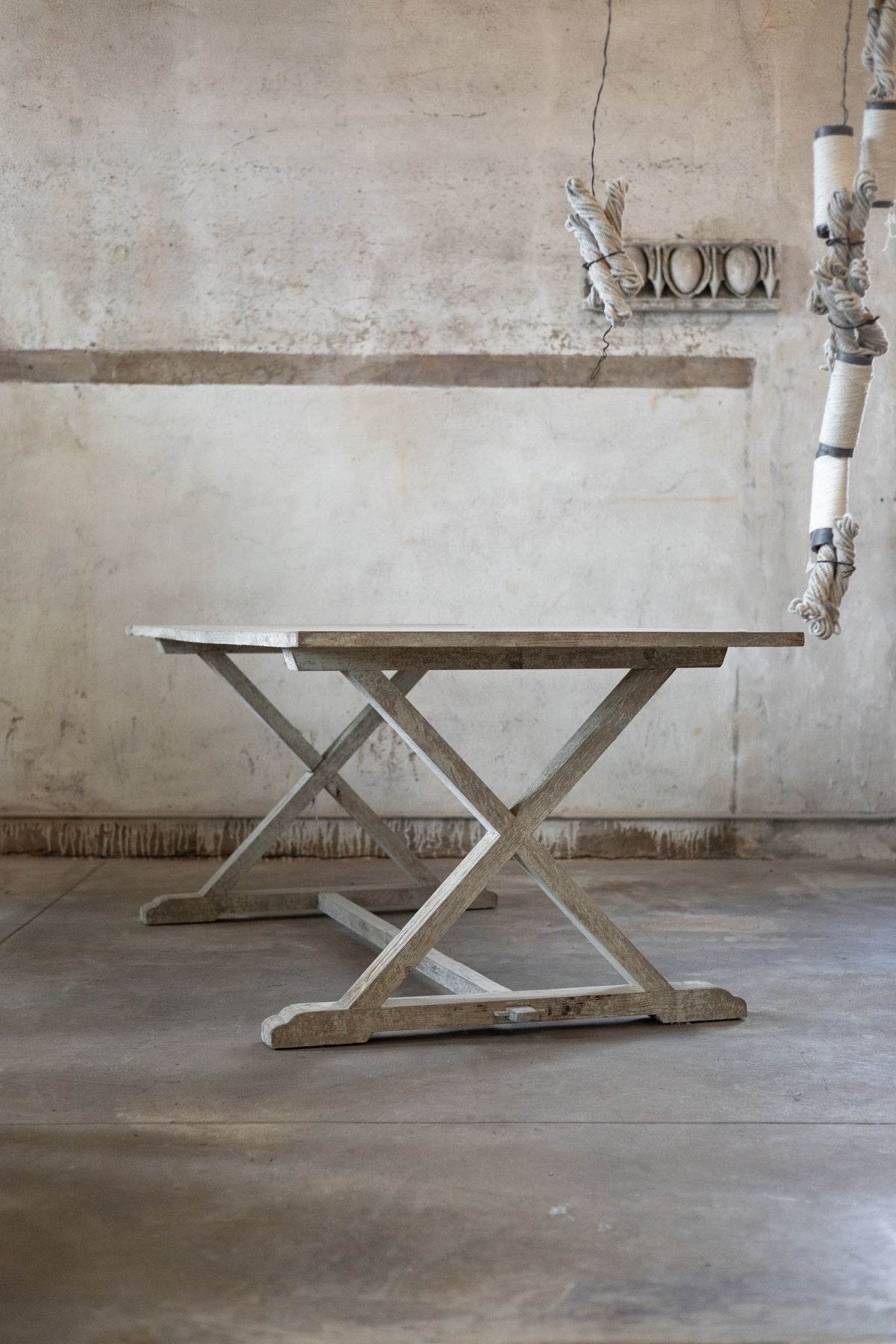 Wooden dining table with X-shaped base in a rustic interior setting