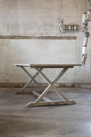 Wooden dining table with X-shaped base in a rustic interior setting