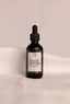 Black bottle of anti-aging body serum with a dropper on a beige background.