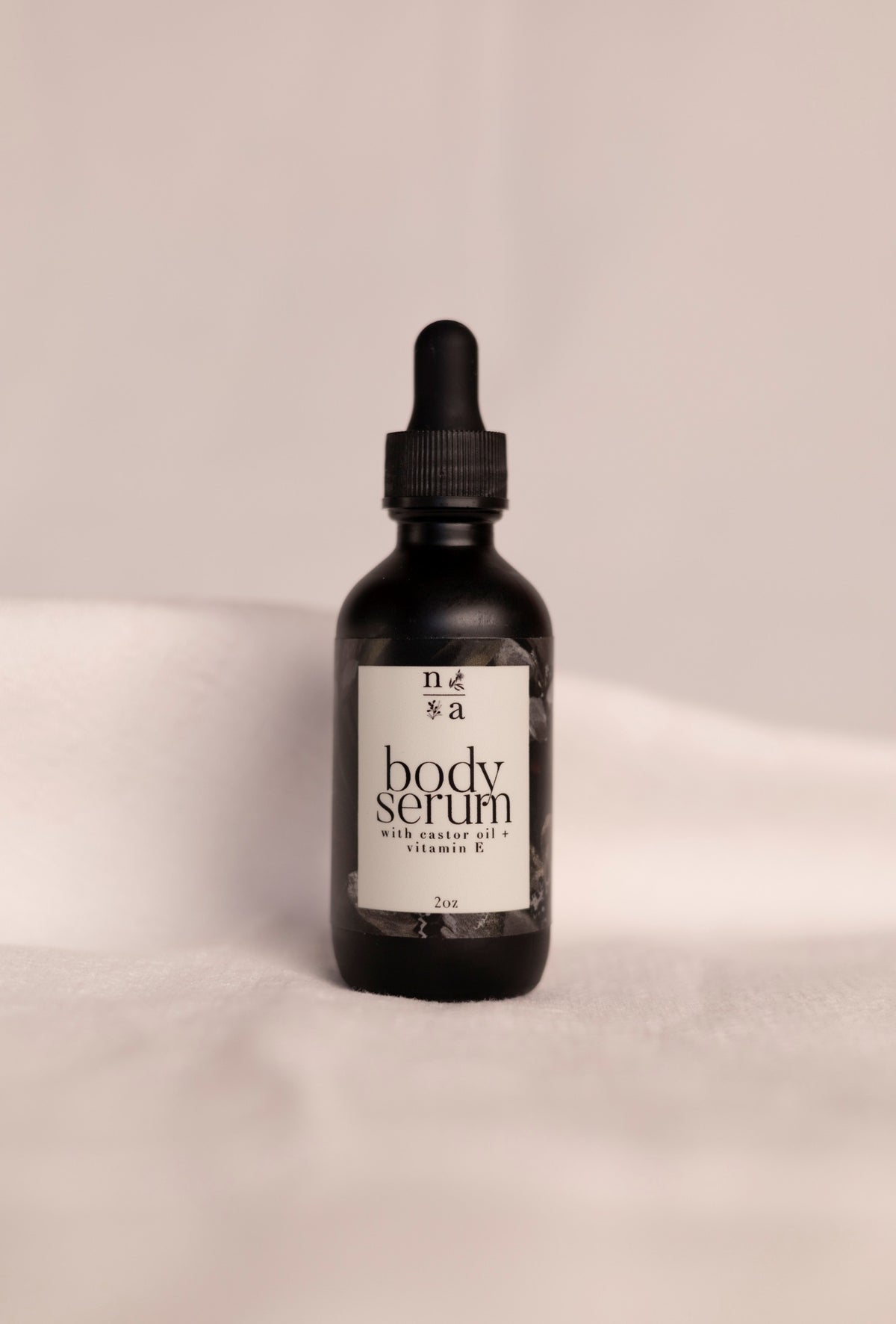 Black bottle of anti-aging body serum with a dropper on a beige background.