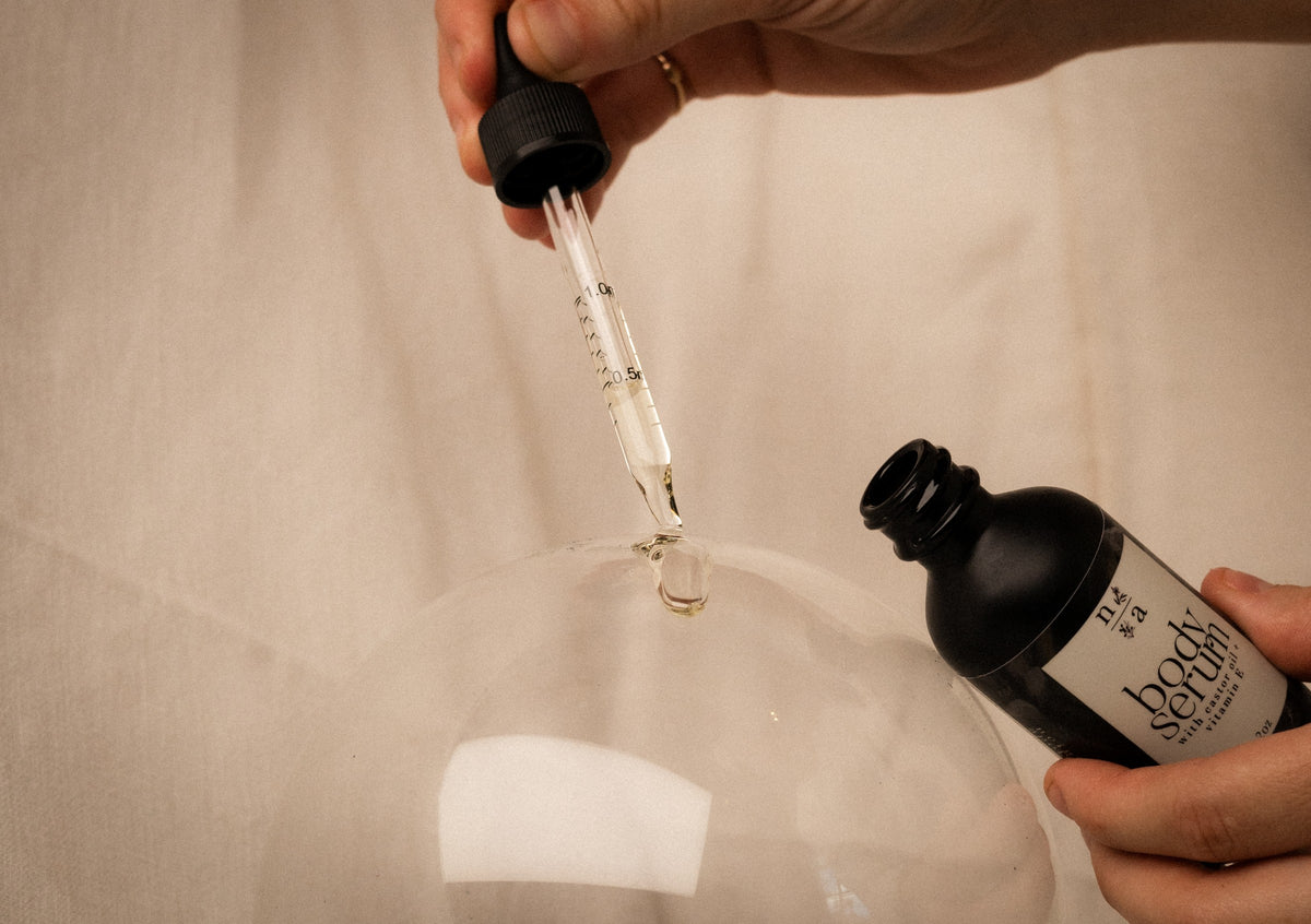 Person using a dropper to apply liquid anti aging body serum from a bottle labeled onto a glass surface to show clear smooth consistency.