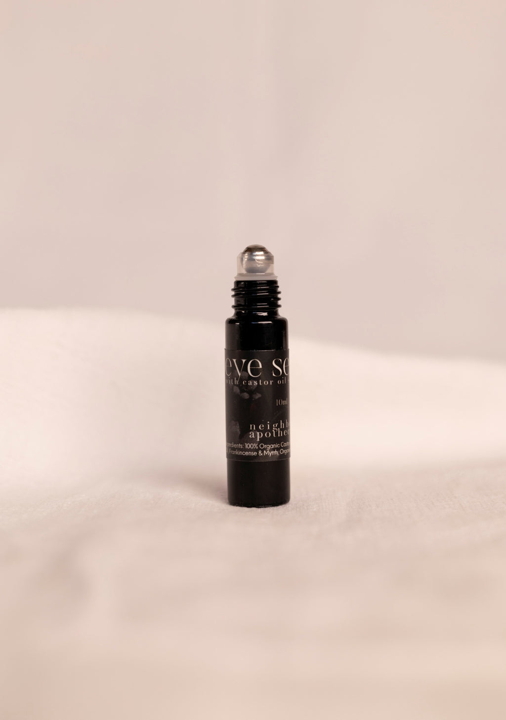 Black rollerball bottle for anti aging eye serum with silver roller ball on a beige background.