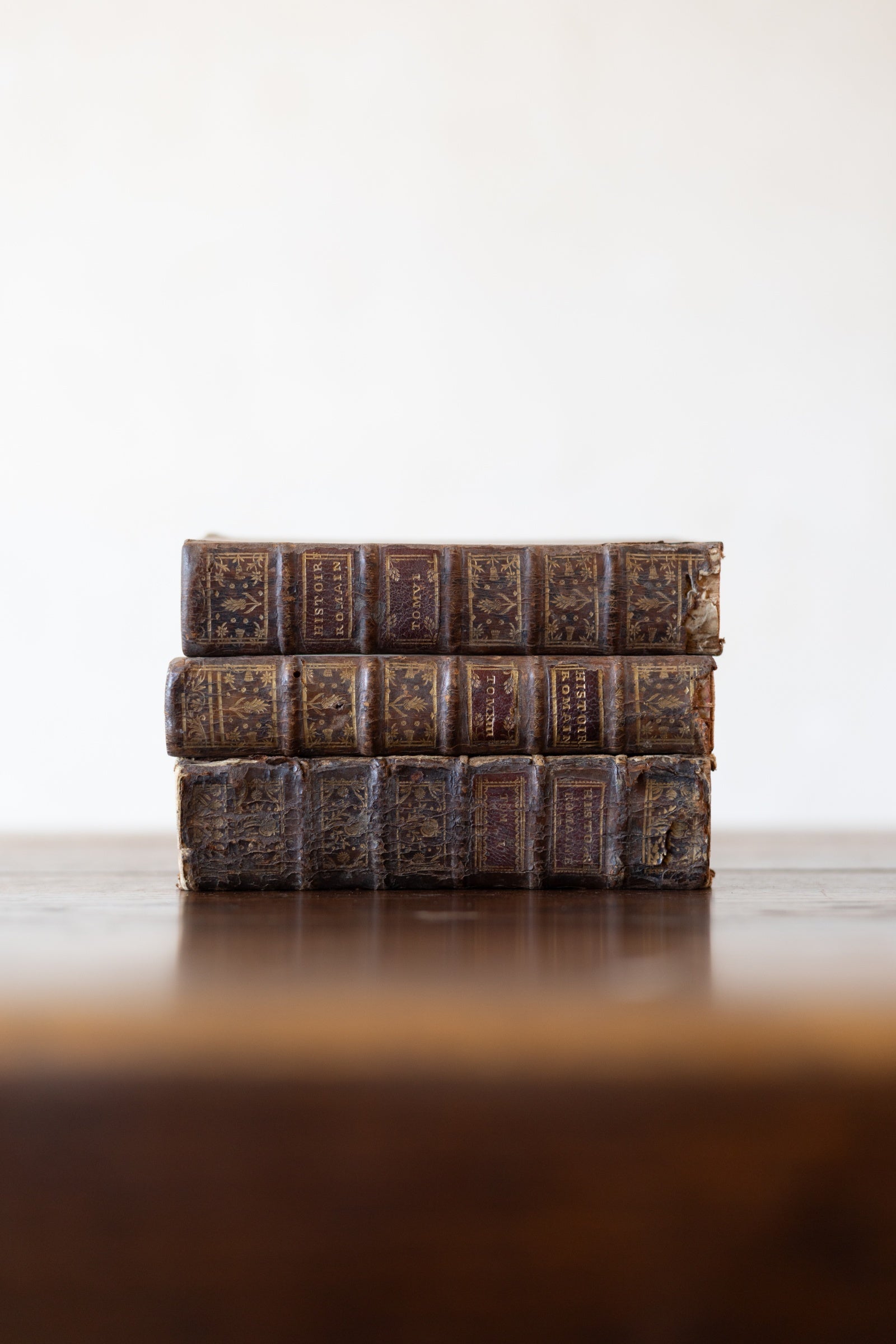 Stack of vintage leather-bound books on a wooden table top with a white background.