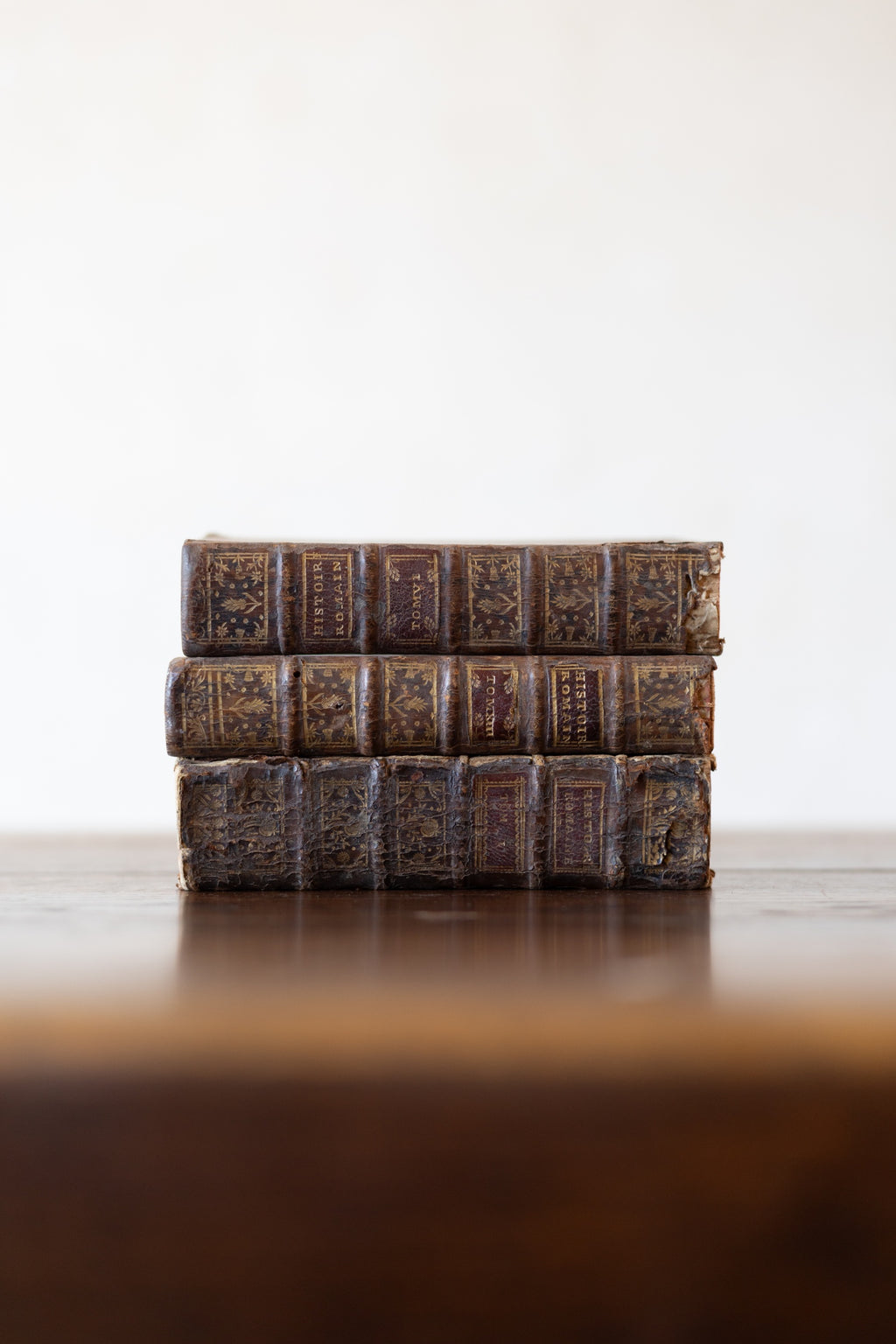 Stack of vintage leather-bound books on a wooden table top with a white background.