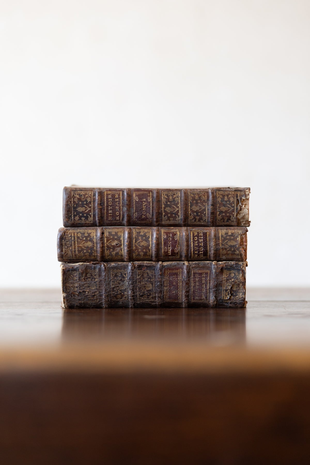 Stack of vintage leather-bound books on a wooden table top with a white background.