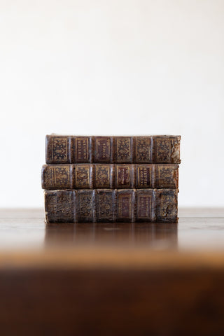 Stack of vintage leather-bound books on a wooden table top with a white background.