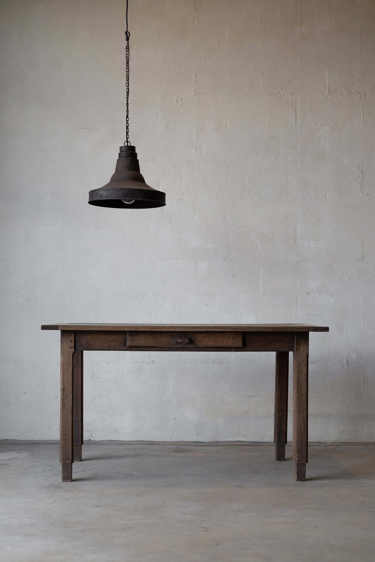 An oak farm table with a rustic finish, a thin tabletop, and a drawer.