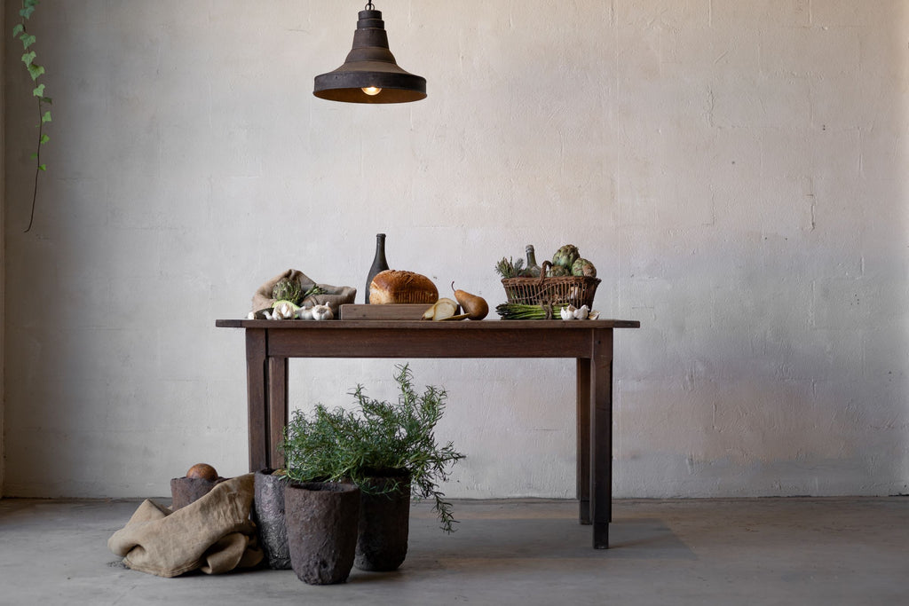 Horizontal image of a dark oak table laden with food, an industrial lamp hanging above it.