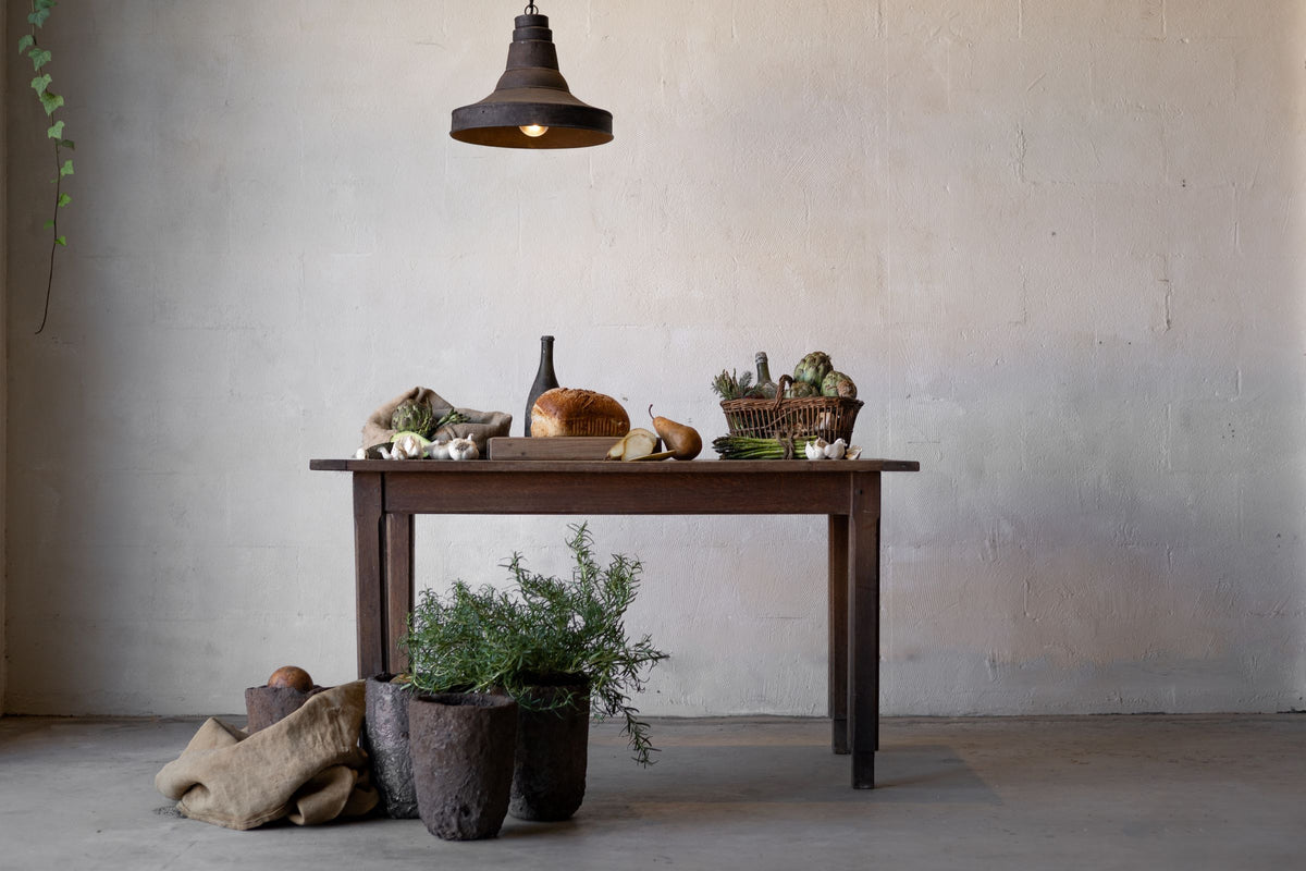 Horizontal image of a dark oak table laden with food, an industrial lamp hanging above it.