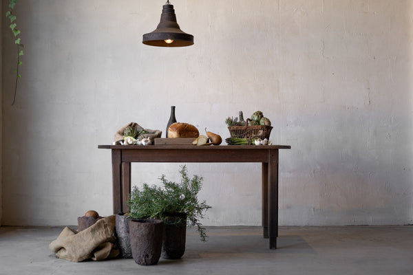 Horizontal image of a dark oak table laden with food, an industrial lamp hanging above it.